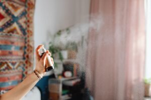 Mão borrifa uma fragrância e a névoa se espalha pelo ar de uma sala com luz natural