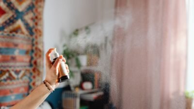 Mão borrifa uma fragrância e a névoa se espalha pelo ar de uma sala com luz natural